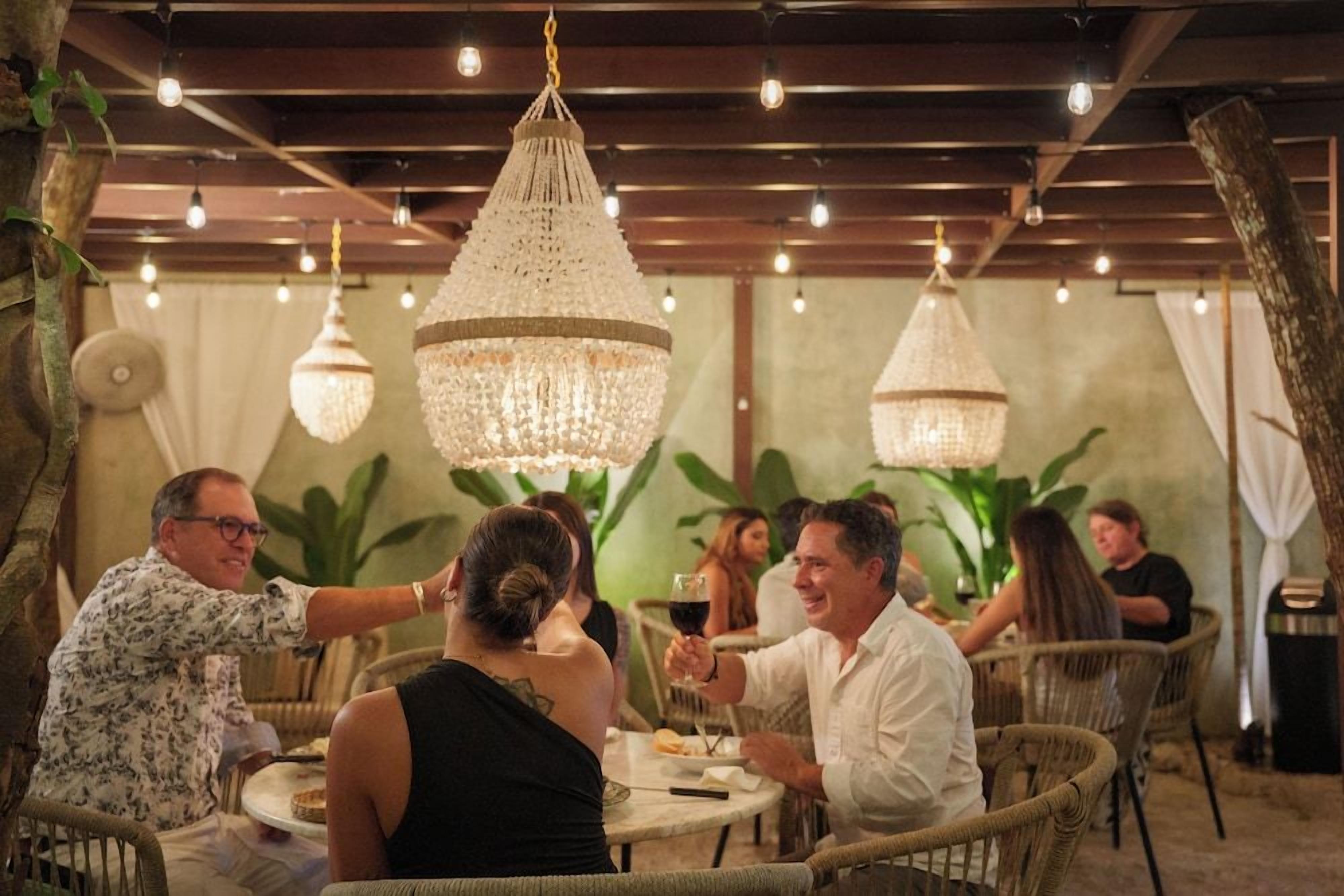 A dining area with wicker chairs, round tables, and hanging crystal chandeliers.