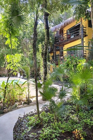 A tropical resort with a pool, lush greenery, and a yellow building with balconies.