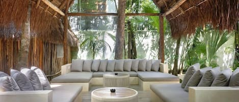 Una habitación con techo de paja, un sofá grande, una mesa de centro redonda y vistas a la vegetación tropical.