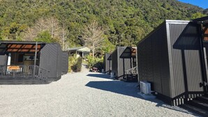 Fileira de cabanas com um caminho de cascalho que leva até elas, com uma montanha arborizada ao fundo.