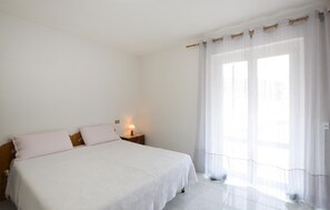 A bedroom with a bed, a nightstand, a lamp, and a window with curtains. - Cozy apartment in Varese Ligure with WiFi (Varese Ligure)