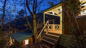 Une cabane avec un escalier en bois menant à une véranda, le tout entouré d’arbres.