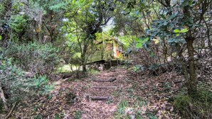 Un pont en bois rustique, situé dans une zone boisée, avec un petit bâtiment de l’autre côté.