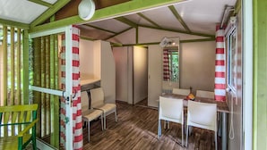 Une petite pièce fermée, dotée d’un plancher en bois, d’une table à manger avec des chaises, d’une petite fenêtre avec des rideaux et d’une porte également munie de rideaux à rayures.