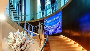 A curved staircase with a handrail, a digital display screen, and a decorative tree. - Shanxi International Hotel (Beijing)