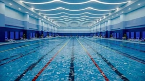 A large indoor swimming pool with multiple lanes, overhead lighting, and lounge chairs along the sides. - Shanxi International Hotel (Beijing)