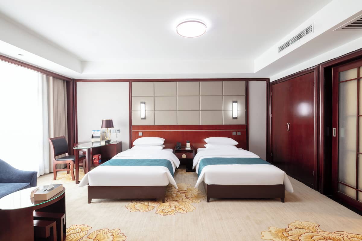 A hotel room with two beds, a desk, a chair, a lamp, and a large mirror.