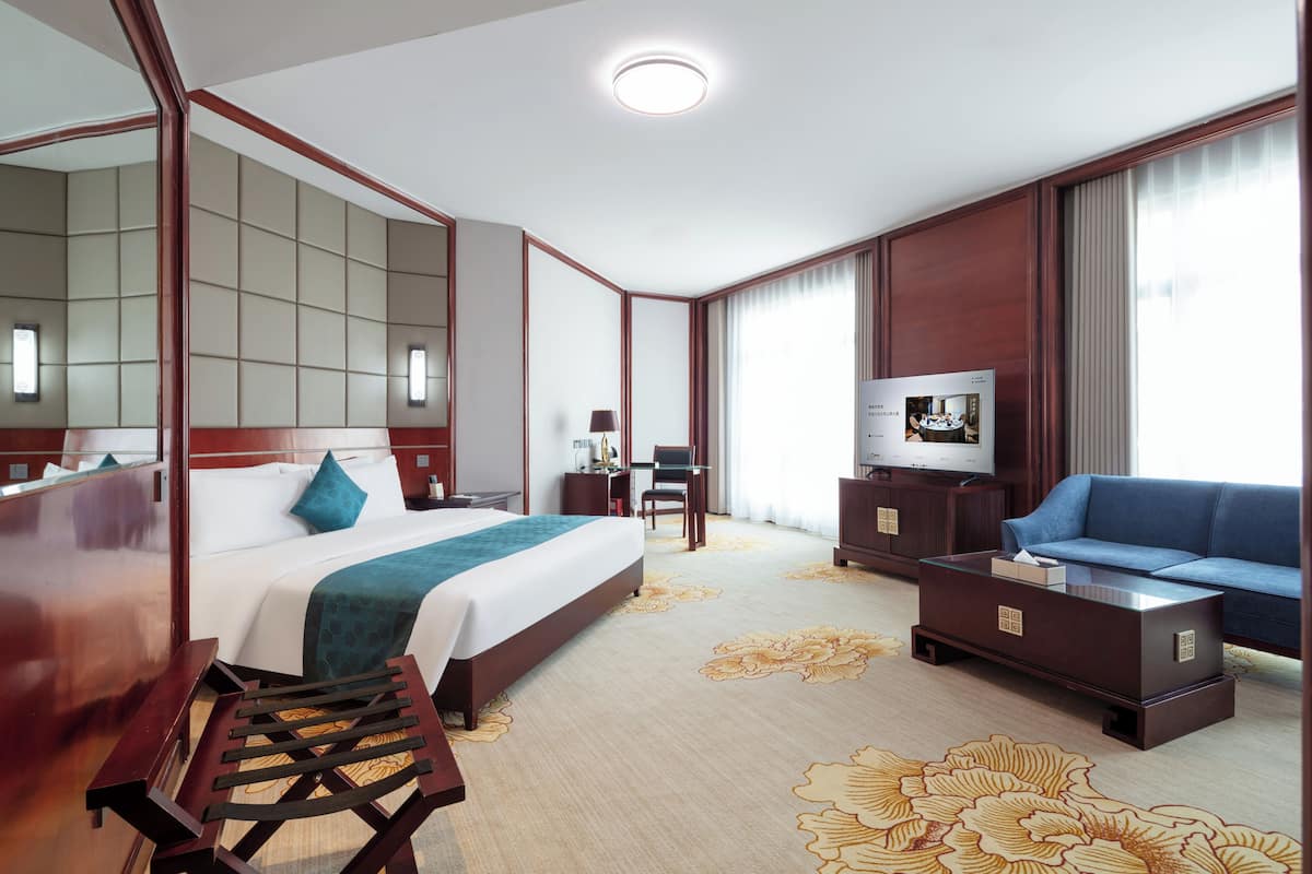 A hotel room with a large bed, a sofa, a TV, and a desk.