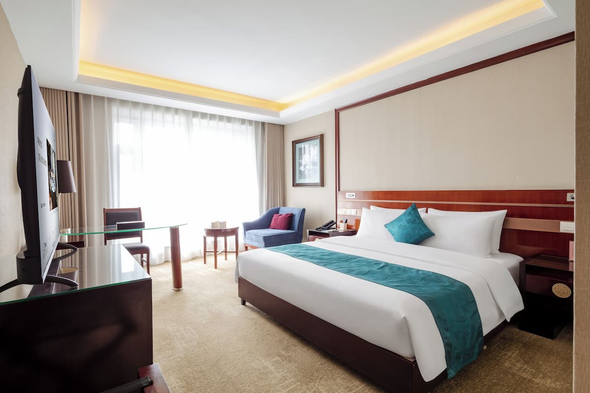 A hotel room with a bed, a desk, a chair, a TV, and a window with curtains.