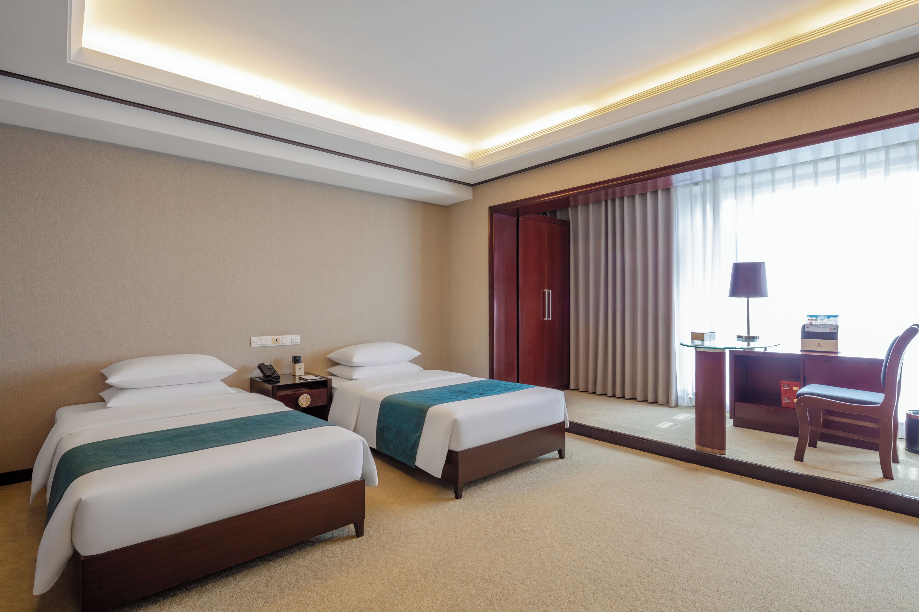 Habitación de hotel con dos camas, un escritorio, una silla y un ventanal con cortinas.