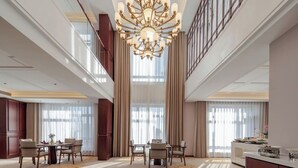 A spacious hotel lobby with a large chandelier, a dining area with tables and chairs, and a view of the city through large windows. - Shanxi International Hotel (Beijing)