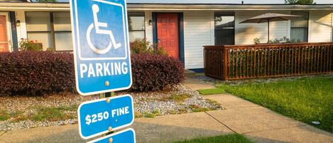 A blue handicapped parking sign with a $250 fine notice and a van accessible sign in front of a building with a red door and a screened porch.