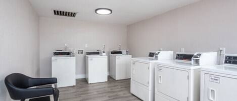 A laundry room with four washing machines and a chair.