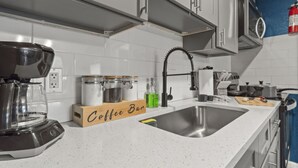 Une cuisine moderne avec des meubles blancs, un évier en acier inoxydable, un coin café et une machine à café.