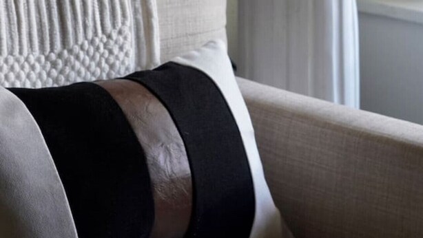 Un fauteuil blanc agrémenté d’un plaid texturé et d’un coussin noir. Un vase blanc contenant des fleurs est posé sur un piédestal blanc au design classique.
