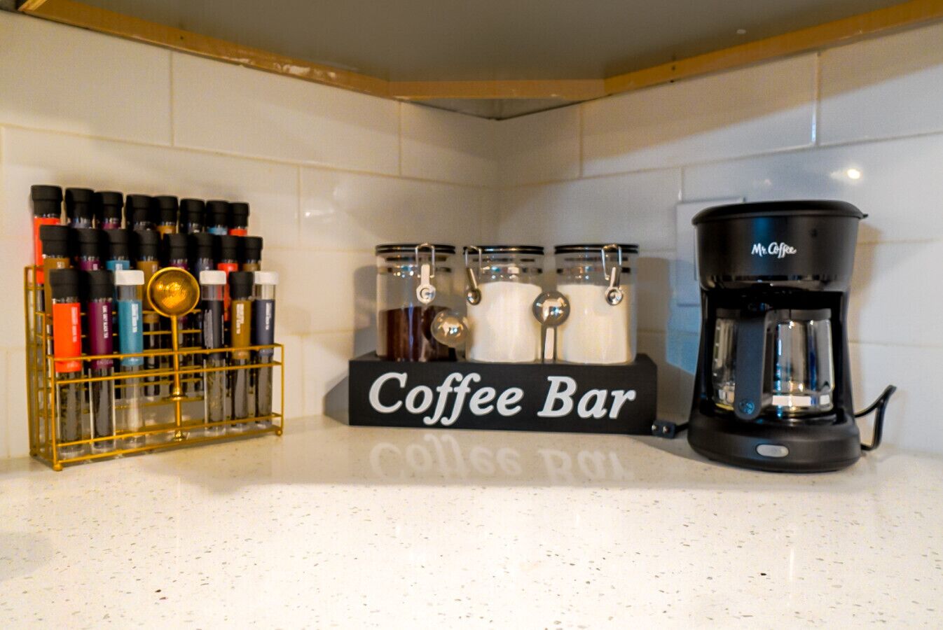 A kitchen counter with a coffee bar setup, including a coffee maker, a coffee grinder, and a spice rack.
