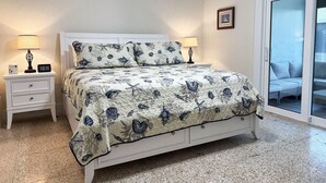 Een slaapkamer met een bed, twee nachtkastjes, een digitaal klokje, een ingelijste foto en een glazen schuifdeur naar een balkon.