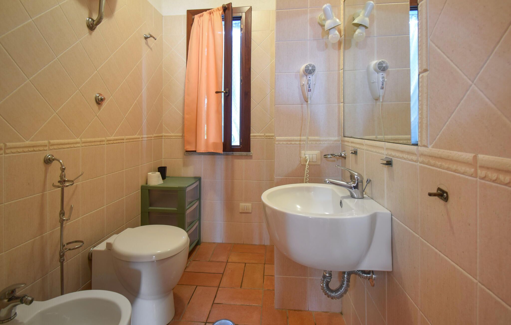 A bathroom with a toilet, bidet, sink, and two hair dryers mounted on the wall.