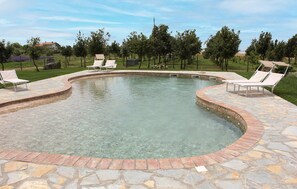 Ein Pool mit gewölbter Kante, umgeben von Steinplatten und weißen Liegestühlen.