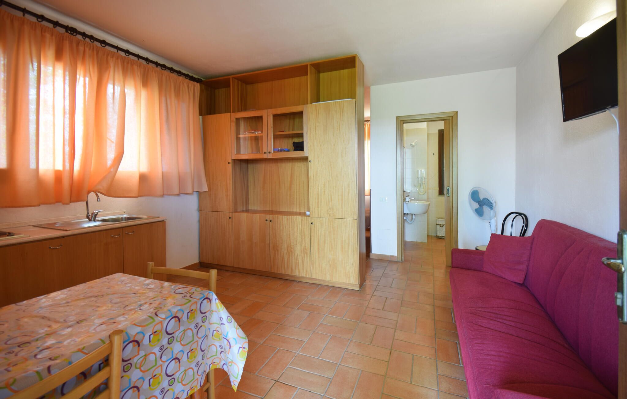 A compact room with a kitchenette, a dining area, a sofa, and a bathroom visible through an open door.
