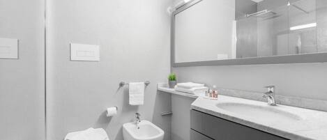 A modern bathroom with a bidet, toilet, and a large mirror above the sink.