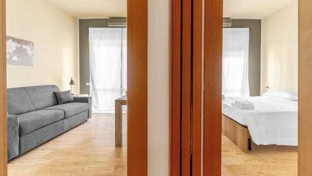 Una habitación de hotel moderna con un sofá gris, un marco de cama de madera y una pequeña mesa.