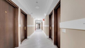Un pasillo largo y estrecho con puertas de madera a ambos lados, paredes blancas y suelo de color claro.