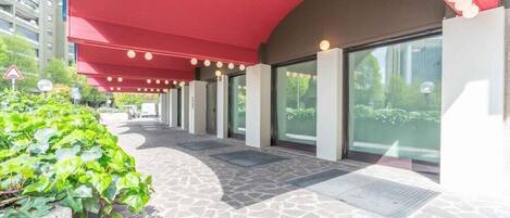 A covered walkway with stone flooring, large windows, and a red canopy.