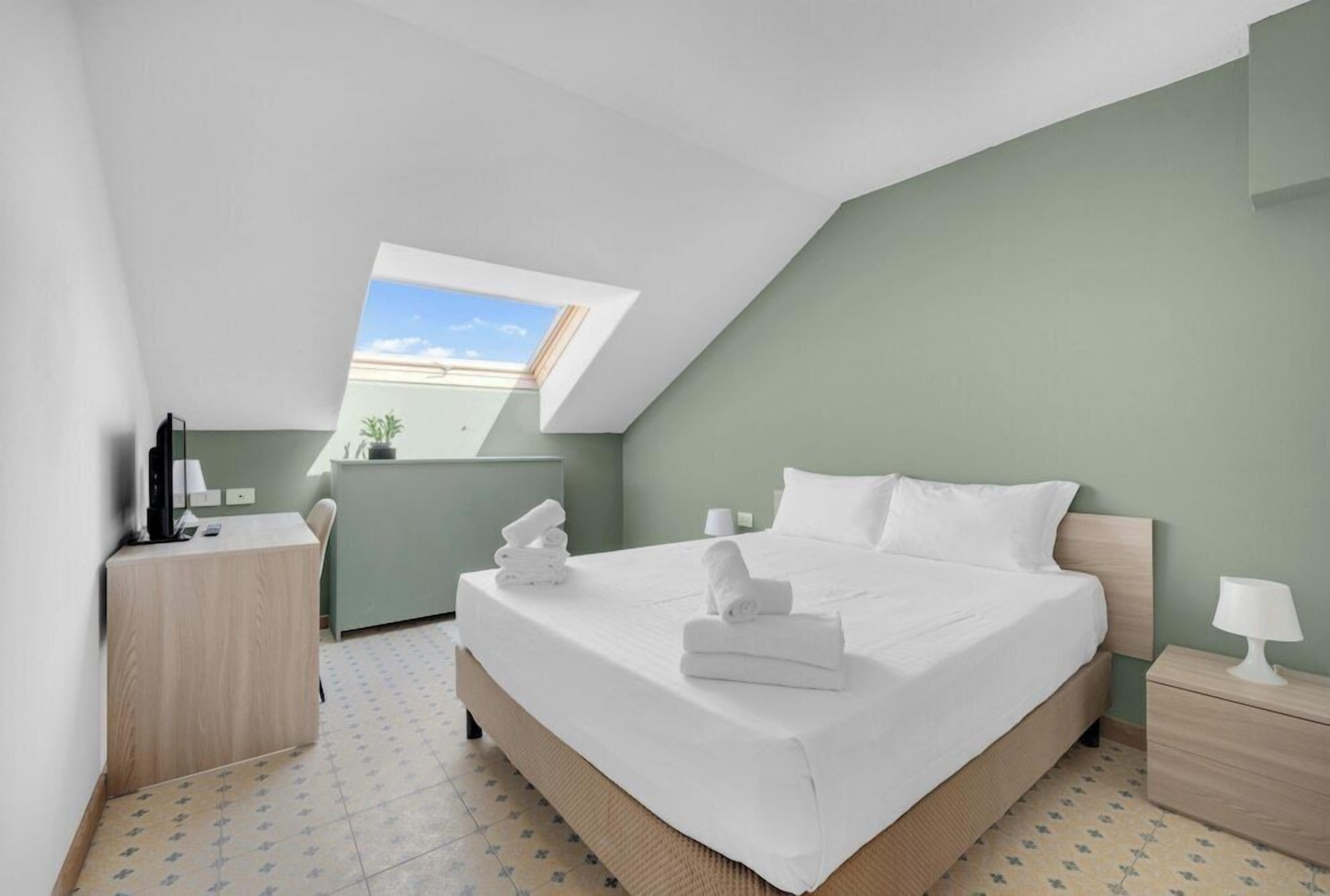 Une chambre à coucher comprenant un lit, un bureau, une chaise, une table de chevet, une lampe et une fenêtre.