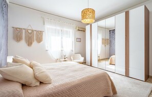 Ein Schlafzimmer mit einem Bett, Nachttischen, einem Sessel, einem Spiegel und einer Pendelleuchte.