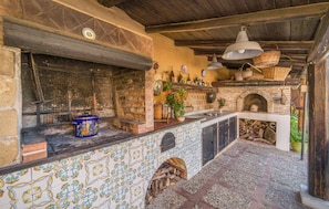 A rustic kitchen with a tiled backsplash, a brick oven, and hanging light fixtures.