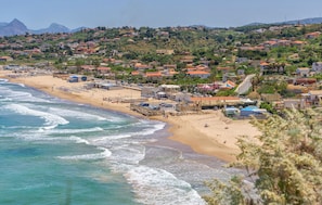 A coastal town with a beach, houses, and wind turbines in the background.