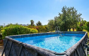 A rectangular swimming pool with a ladder, surrounded by lush greenery and trees.