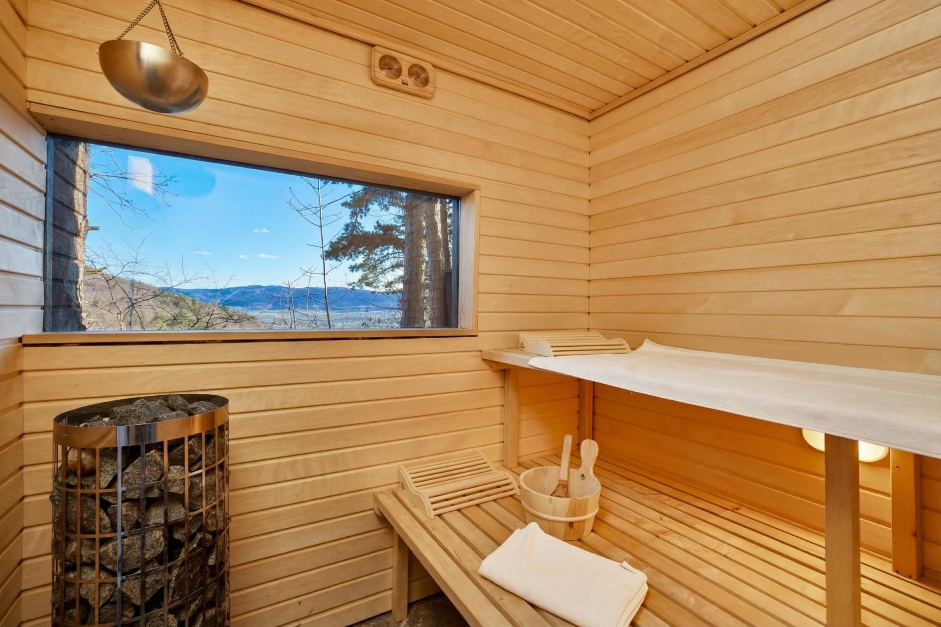A wooden sauna room with a window, a bench, a towel, and a bucket.