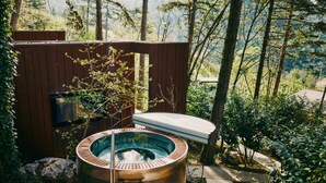 Ein Whirlpool in bewaldeter Landschaft mit einer Holzterrasse und Blick auf Bäume.