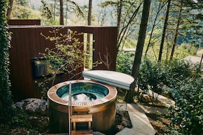 Ein Whirlpool in bewaldeter Landschaft mit einer Holzterrasse und Blick auf Bäume.