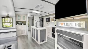 A modern RV interior with a kitchenette, a dining area, and a TV mounted on the wall.