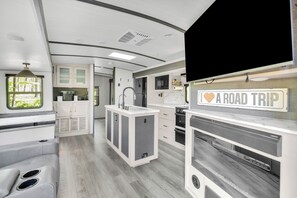 Een modern RV-interieur met een kitchenette, een eethoek en een aan de muur bevestigde televisie.
