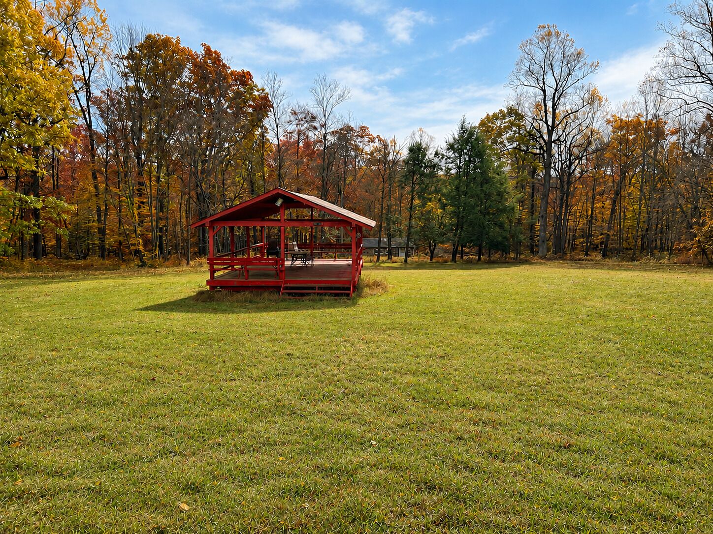 A red wooden cabin with a porch, surrounded by a grassy field and trees with autumn foliage.