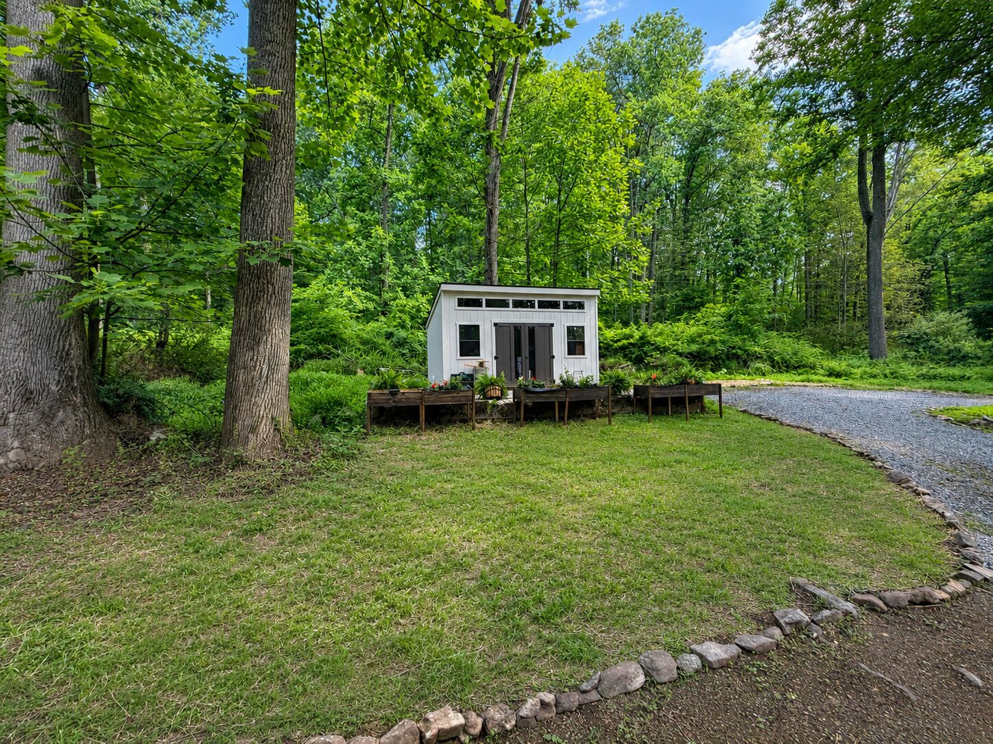 A small white cabin with a door and windows, surrounded by a grassy area and trees.