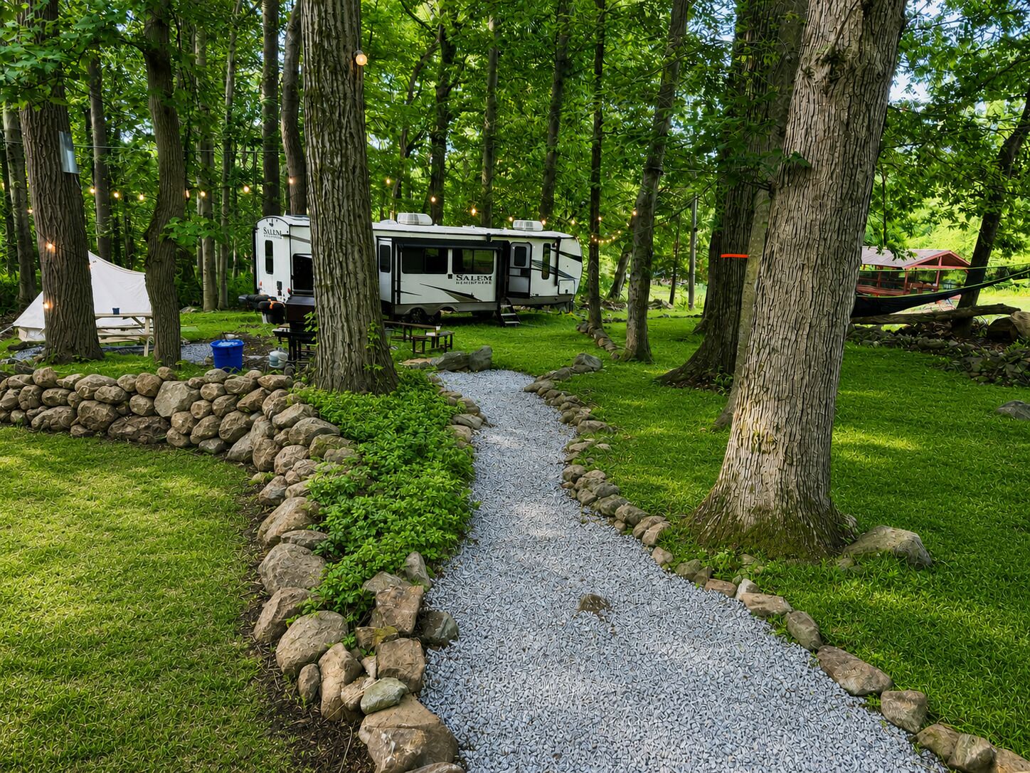 Un chemin de gravier mène à un camping-car blanc sur lequel on peut lire le mot « SALEM », le tout étant entouré d’arbres et d’un espace aménagé pour pique-niquer.