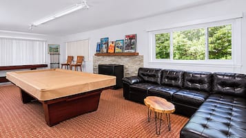 A room with a pool table, a black leather sofa, a small wooden table, and a fireplace with framed pictures.