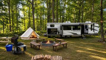 A campsite with a tent, RV, picnic tables, a fire pit, and a grill.