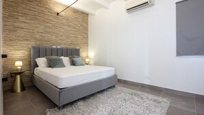 A modern bedroom with a stone wall, a grey bed, fluffy pillows, and a grey rug. - Amazing home in Salemi (Salemi)