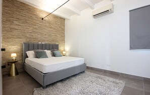 A modern bedroom with a stone wall, a grey bed, fluffy pillows, and a grey rug. - Amazing home in Salemi (Salemi)