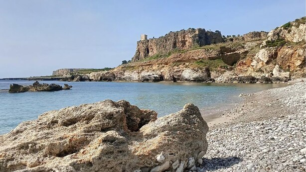 Ein felsiger Strand mit einer hohen Klippe und einem Gebäude obenauf.