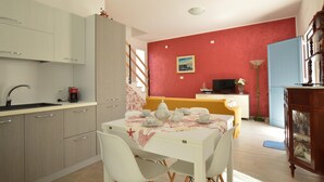 Eine kompakte Küche mit modernen Geräten, ein Essbereich mit Tisch für zwei Personen und eine Wand in Rot als Akzent.