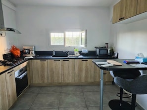 A kitchen with wooden cabinets, a gas stove, a microwave, a sink, and a window. - Le Petit Maraîcher: Terrace & Total Tranquility (Puget-sur-Argens)