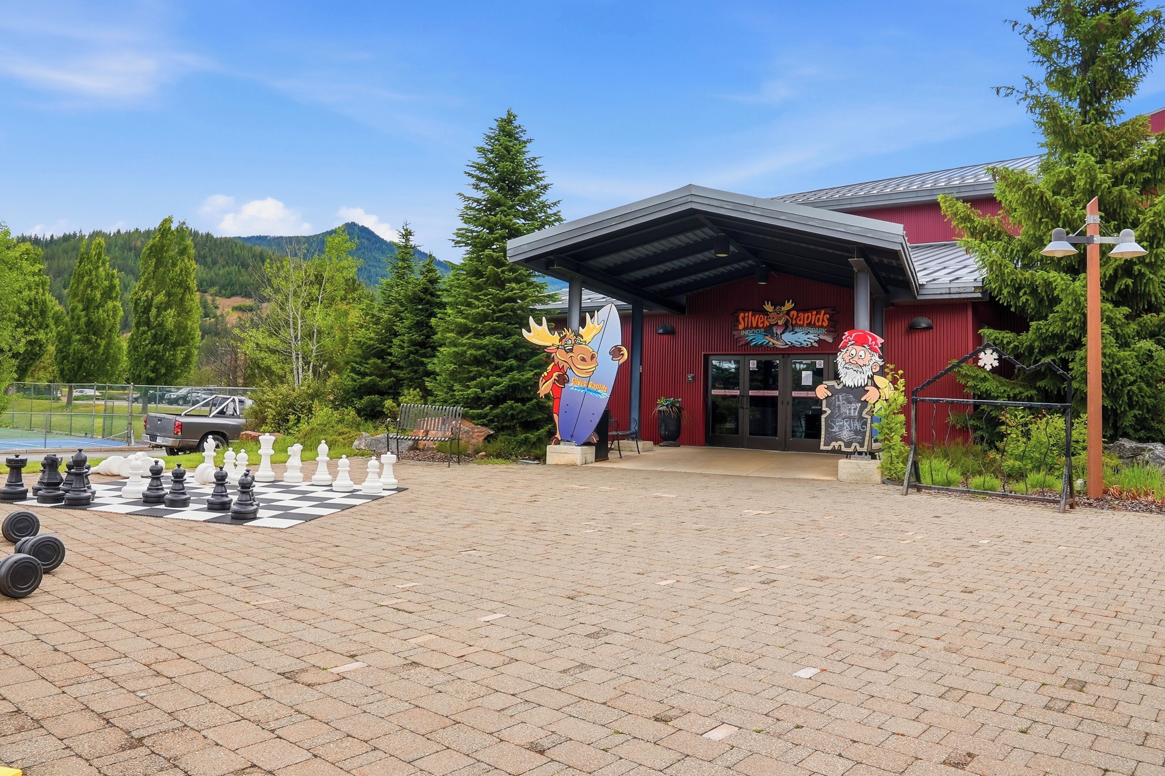 A building with a red exterior, a large chessboard in the foreground, and a mountain backdrop.