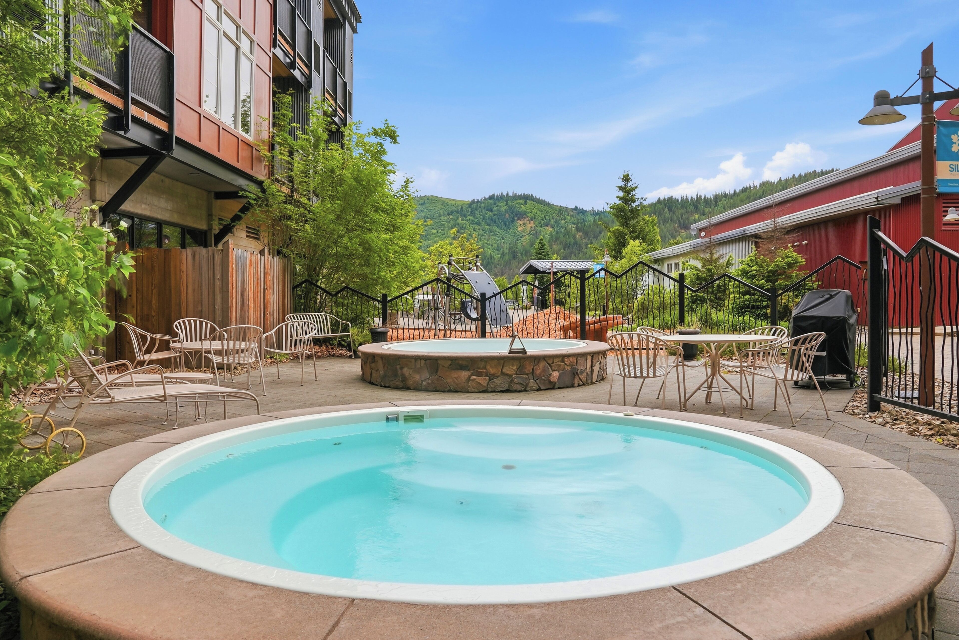 A swimming pool with a stone surround, outdoor seating, and a view of a forested hill.